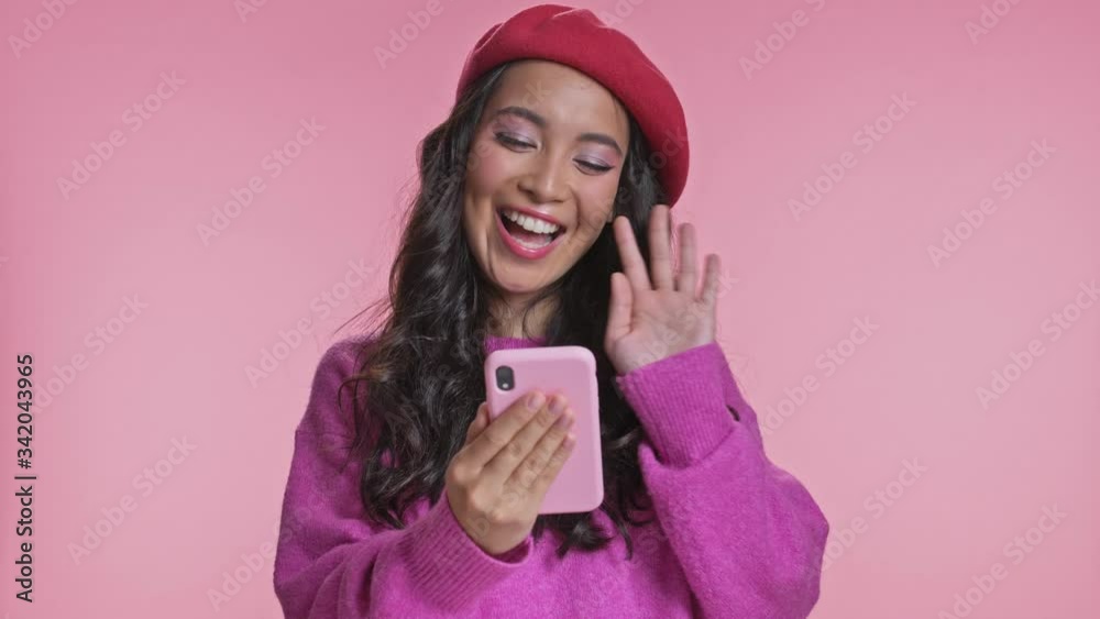 Young optimistic asian woman posing isolated over pink wall background talking by mobile phone. Young optimistic asian woman posing isolated over pink wall background talking by mobile phone.