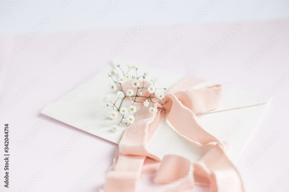 Envelope on a white-pink background with peach silk ribbon and pink flowers. Wedding invitation. Mother's day card. Place for text. Copy space