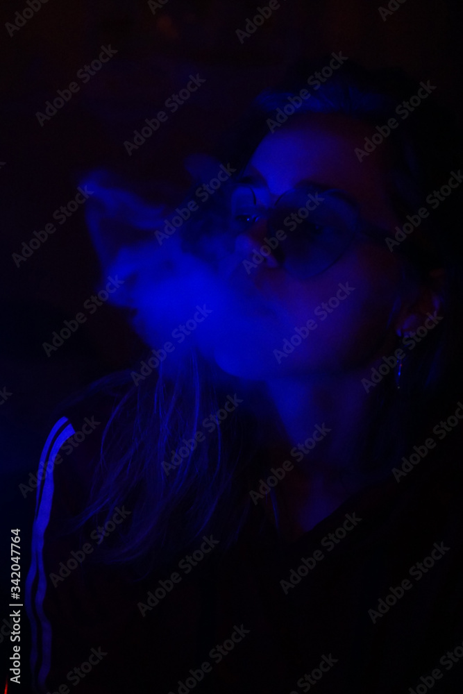 Close up vertical portrait of vaping girl in neon blue light Close up vertical portrait of vaping girl in neon blue light