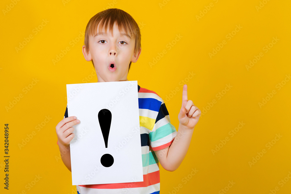 Cute boy holding paper sheet with exclamation mark. Thoughtful child over yellow background. New idea for school project. Cute boy holding paper sheet with exclamation mark. Thoughtful child over yellow background. New idea for school project.