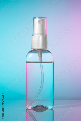 One small bottle of antibacterial hand sanitizer alcohol mist spray. Antiseptic liquid in transparent plastic container with white atomizer pump on gradient blue magenta background, no label.