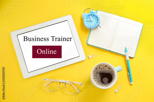 Modern tablet with text BUSINESS TRAINER ONLINE on yellow background, flat lay
