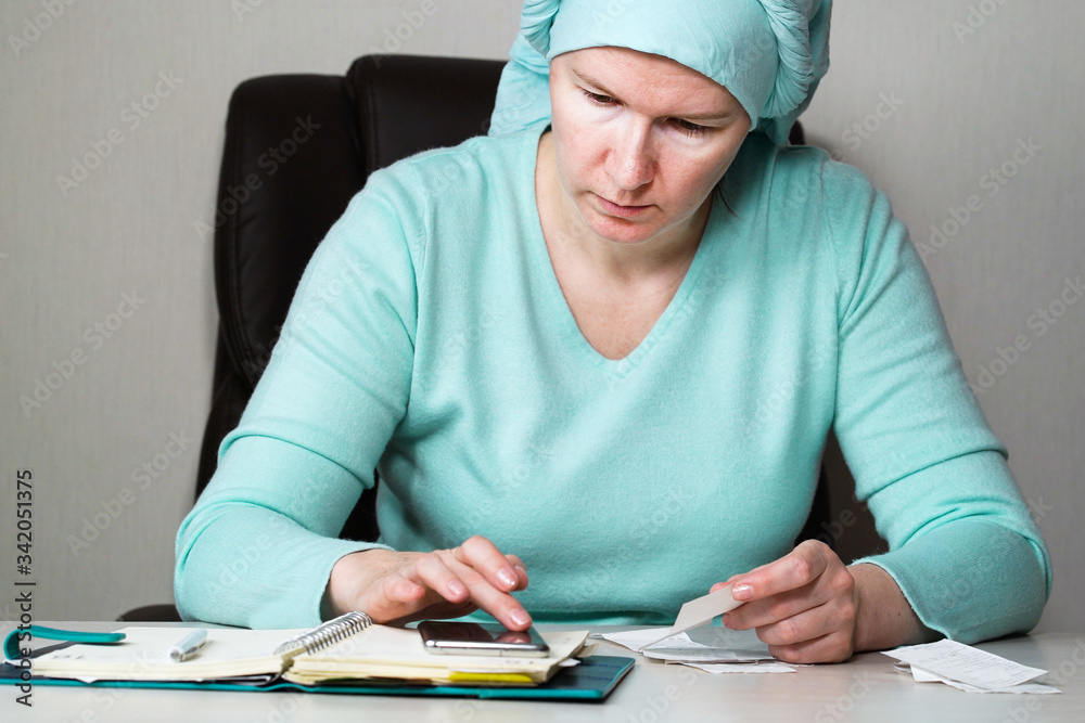 Woman in headscarf checking bills and writing down expenses Woman in headscarf checking bills and writing down expenses