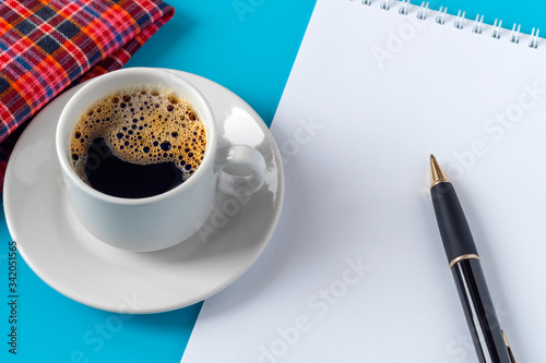 notebook with a white sheet and a pen. white sheet of paper is a negative space. cup of coffee and a checkered napkin of red. free space for text