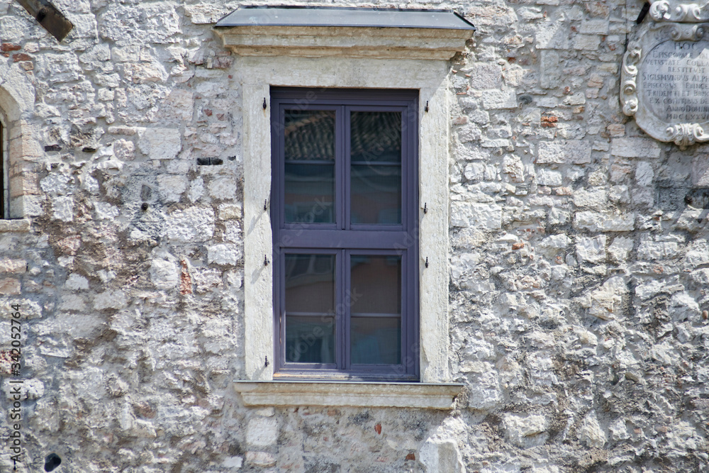 Italian window on the old castle stone wall facade with wooden violet color frame Italian window on the old castle stone wall facade with wooden violet color frame