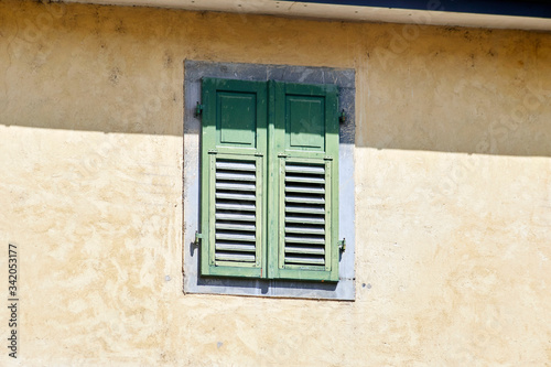 Italian window on the yellow wall facade with closed green color wooden classic shutters