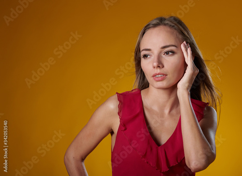 Female in red dress on yellow background natural expression hand next to the face