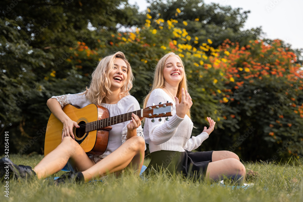 Portrait of caucasian young women sitting in the park outdoor and playing a guitar sing a song together with happiness