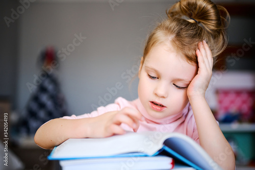Little caucasian schoolgirl, reading books, doing homework. Training books, notebooks and globe at the table. Distance learning concept, online education
