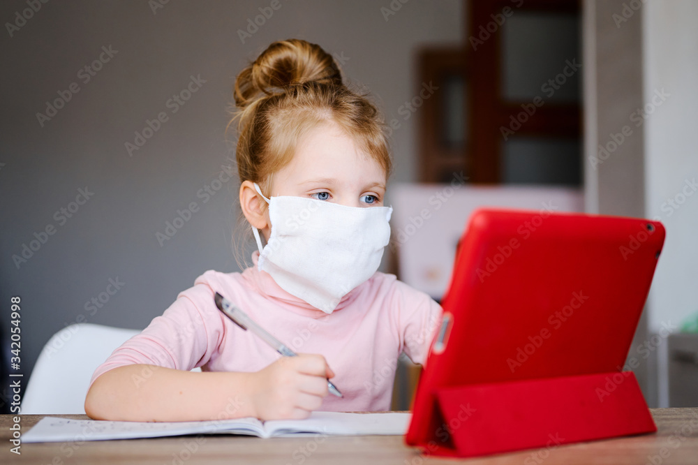 Distance learning online education. Schoolgirl in medical mask studying at home with digital tablet and doing school homework. Training books and notebooks on table Distance learning online education. Schoolgirl in medical mask studying at home with digital tablet and doing school homework. Training books and notebooks on table