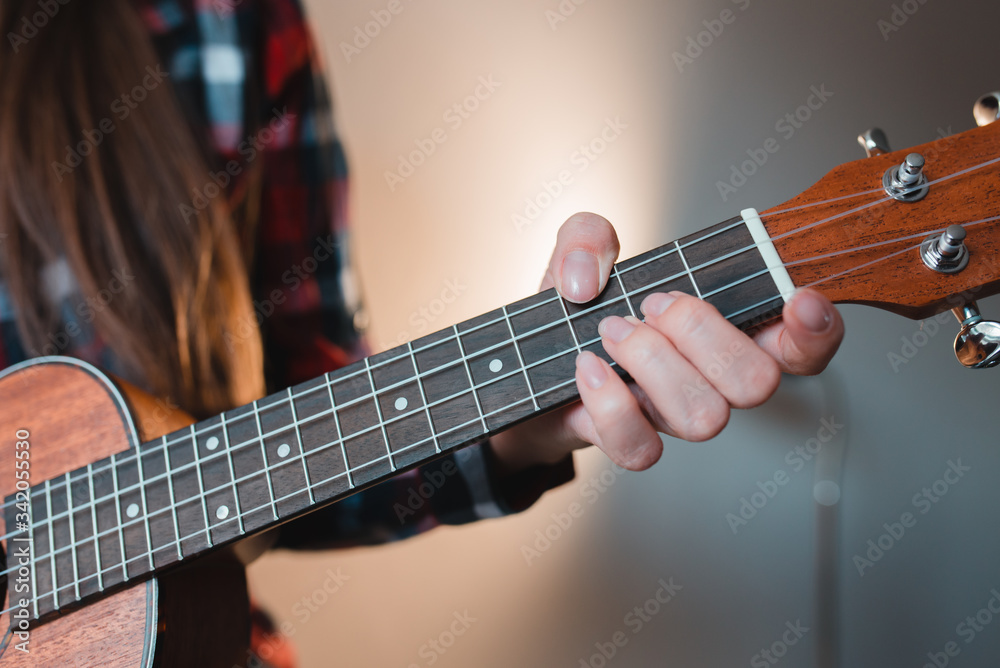 Obraz premium Young girl with long hair in a red shirt plays on ukuded sitting at home.