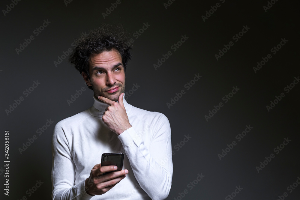 Portrait of an excited casual curly man with new ideas standing with raised hand and holding his phone Portrait of an excited casual curly man with new ideas standing with raised hand and holding his phone