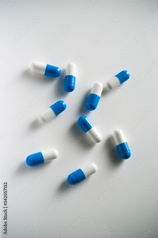 Several blue and white pills scattered around on top of a white tabletop. Several blue and white pills scattered around on top of a white tabletop.