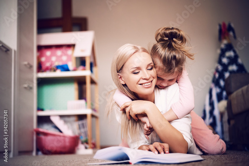 Young mother is relaxing and having fun at home with her daughter, a woman is reading a book to her child, a strong family, love, concept.