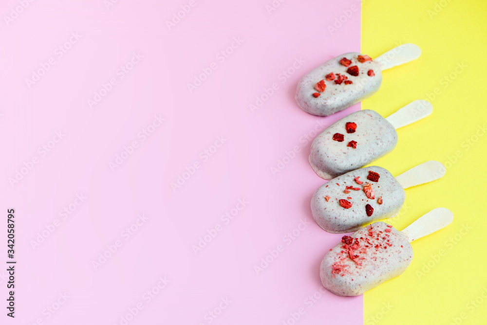 Ice cream on stick coated with white chocolate and red sprinkles of strawberry . Yellow and pink background. Copy spa?e. Summer food concept