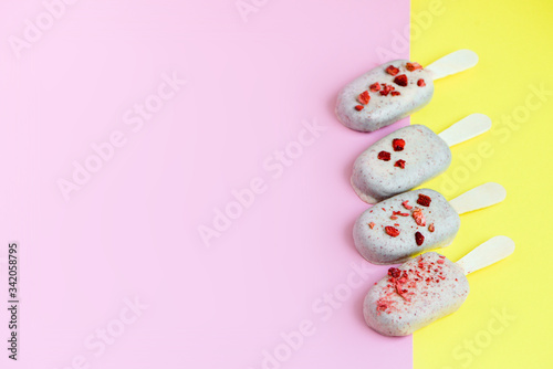 Ice cream on stick coated with white chocolate and red sprinkles of strawberry . Yellow and pink background. Copy spa?e. Summer food concept