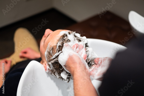 Barber washes young man hair in barbershop, lots of foam