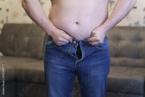 An overweight man tries to wear pants that do not fit his size