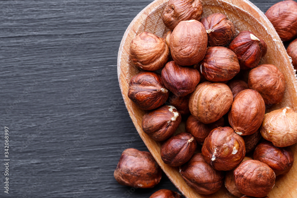 Hazelnuts in wooden bowl. Assortment of nuts - cashew, hazelnuts, walnuts, pistachio, pecans, pine nuts, peanut, raisins on black background. Top view. Hazelnuts in wooden bowl. Assortment of nuts - cashew, hazelnuts, walnuts, pistachio, pecans, pine nuts, peanut, raisins on black background. Top view.