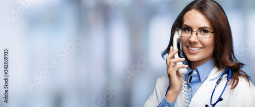 Portrait picture of happy smiling young doctor talking on phone, blurred office background. Copy space for some sign, slogan or advertising text. Medical call center service. photo