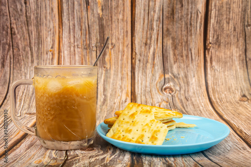 Cup of cold coffee with Crackers on a plate on wooden background.