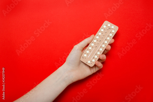 Girl holds birth control pills in her hands. Contraception. Red background, place for text.
