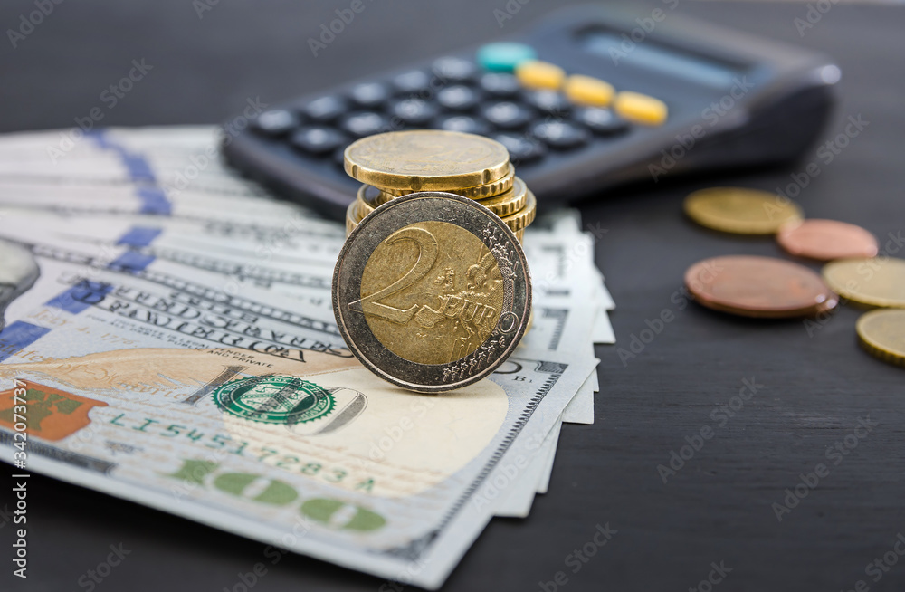 2 euro coin in a hand against the background of dollars and a calculator. Business concept. Black background.