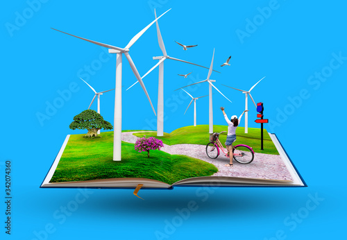 Open book with Young happy girl riding bicycle on meadow in a wind turbine, The eco power concept.