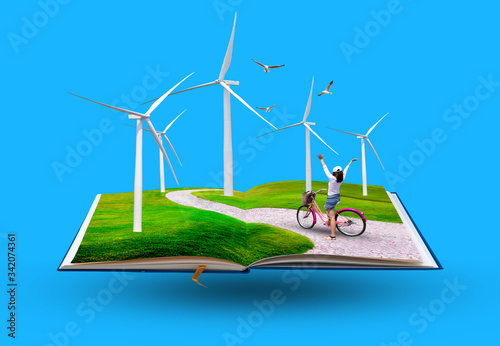 Open book with Young happy girl riding bicycle on meadow in a wind turbine, The eco power concept.