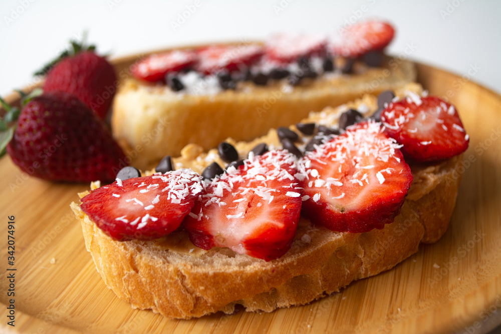 Peanut butter spread toasts with chocolate chips, strawberries, coconut flakes and homemade bread on a wooden plate Peanut butter spread toasts with chocolate chips, strawberries, coconut flakes and homemade bread on a wooden plate