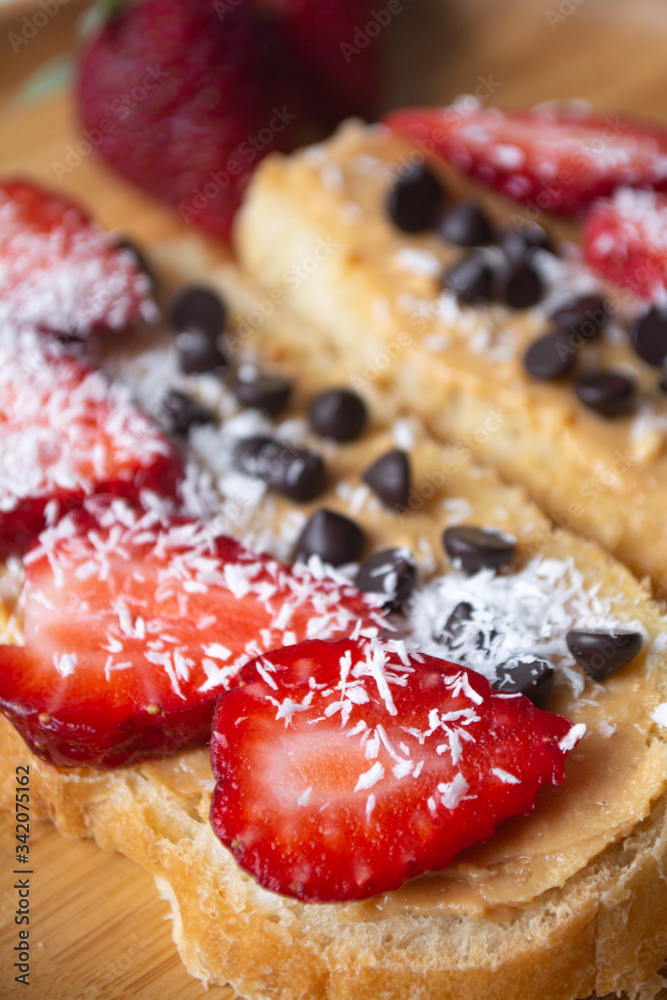 Peanut butter spread toasts with chocolate chips, strawberries, coconut flakes and homemade bread on a wooden plate Peanut butter spread toasts with chocolate chips, strawberries, coconut flakes and homemade bread on a wooden plate