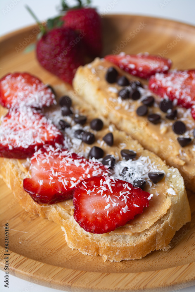 Peanut butter spread toasts with chocolate chips, strawberries, coconut flakes and homemade bread on a wooden plate Peanut butter spread toasts with chocolate chips, strawberries, coconut flakes and homemade bread on a wooden plate