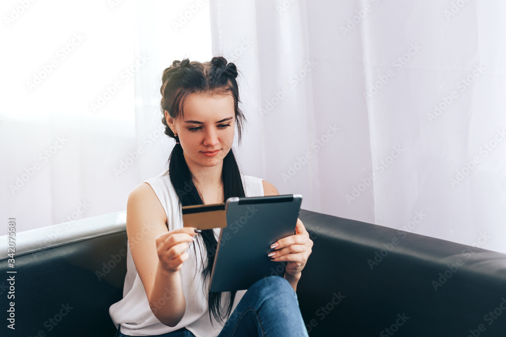 A young girl sits in chair with tablet and pays bills, online purchases, payment for goods during quarantine, payment of services during isolation A young girl sits in chair with tablet and pays bills, online purchases, payment for goods during quarantine, payment of services during isolation