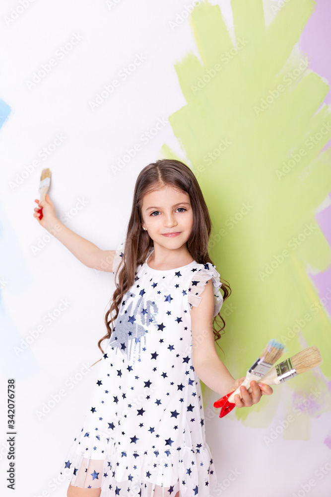 girl showing a paintbrush and smiling. little girl with brush on white wall. girl showing a paintbrush and smiling. little girl with brush on white wall.