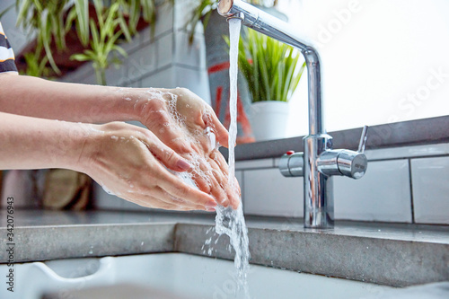 Washing hands. This is an example of a woman thoroughly washing her hands, with a tap running, showing really good, clean hands. This image has plants in the background, and shot with natural light
