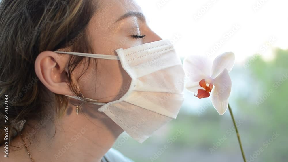 Young girl in medical protective mask sniffs an orchid flower Young girl in medical protective mask sniffs an orchid flower