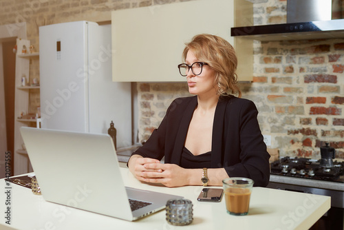 A young woman in glasses works remotely on a laptop in her kitchen. A girl with braces gesturing while talking to her colleagues on a video conference at home. A lady studying online on a webinar