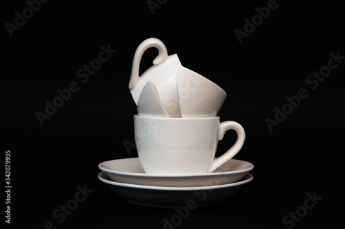 a tower of two small cups, a white whole cup and a broken cup on a black background and place for text.