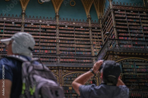 Tourists in the library take photos of the interior against the background of high shelves with books. A large number of books on the shelves.
