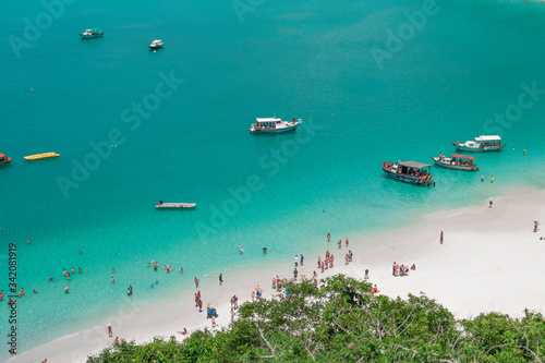 People relax on the beach, tourist boats in the ocean. Top view of the clear azure surface of the ocean (bay), boats and a sandy beach.