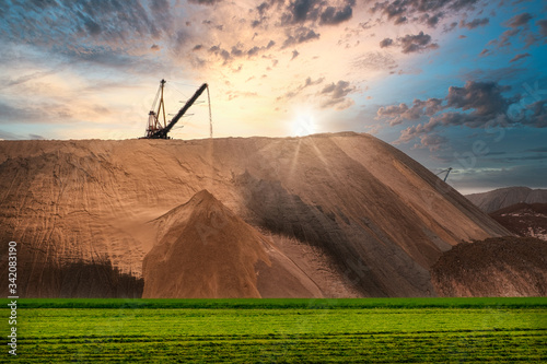 Extracting and mining potassium and magnesium salts.Large excavator machine and Huge mountains of waste ore in the extraction of potassium against the backdrop of a dramatic sunset sky. 