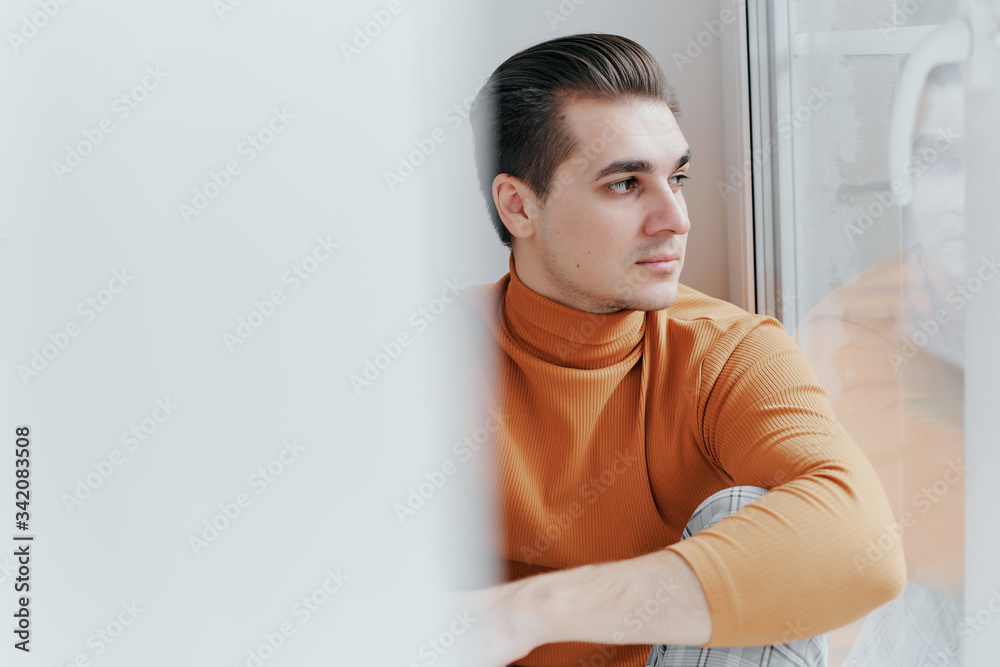 A young guy is sitting on the window and looking at the street A young guy is sitting on the window and looking at the street
