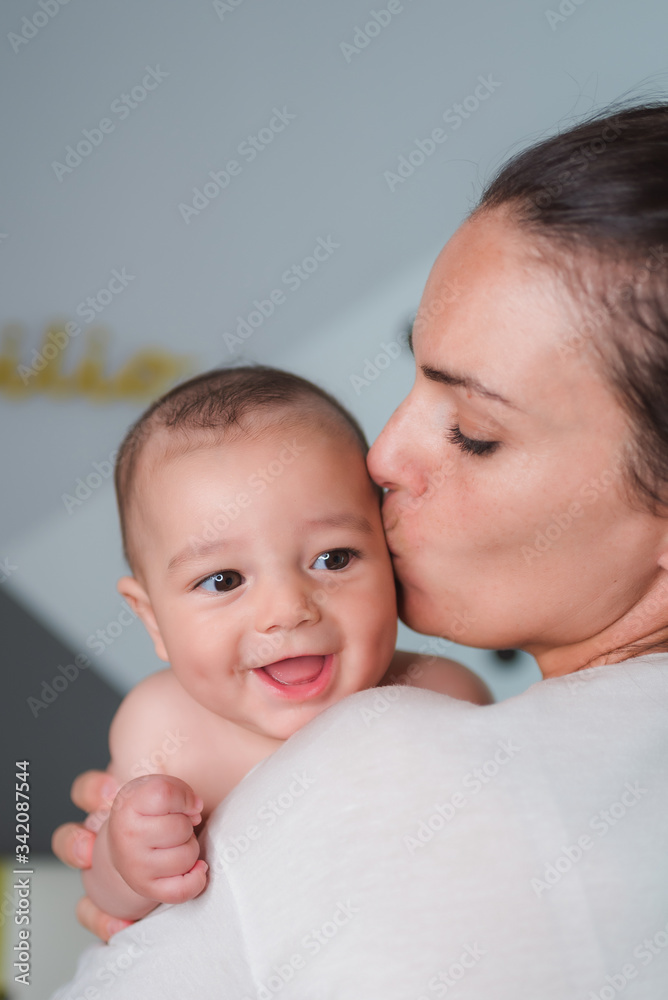 Side view of satisfied young mother in casual wear laughing with content baby in arms during sunny morning Side view of satisfied young mother in casual wear laughing with content baby in arms during sunny morning
