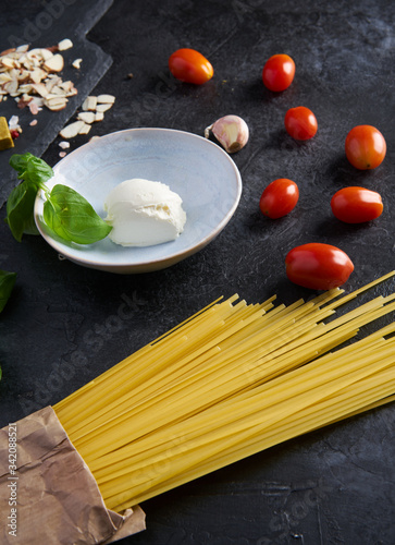 A set of products for an Italian dinner: spaghetti pasta, cherry tomatoes, basil, garlic, cream cheese on a black textured background. Dinner Set Food Delivery