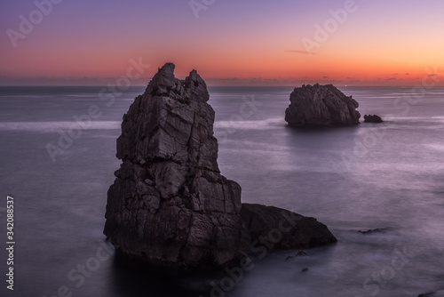 From above picturesque scenery of rough rocks among calm blue sea under colorful evening sky with sun beams breaking through clouds during twilight Costa Brava, Spain