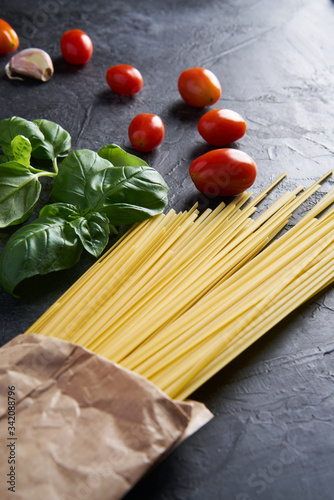 A set of products for an Italian dinner: spaghetti pasta, cherry tomatoes, basil, garlic, cream cheese on a black textured background. Dinner Set Food Delivery