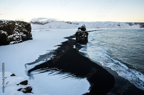 Waves crashing in onshore on Reynisfjara beach and volcanic sand in Iceland. Stunning basalt sculpture columns covered by snow raise up from the sea. Iceland, Europe.