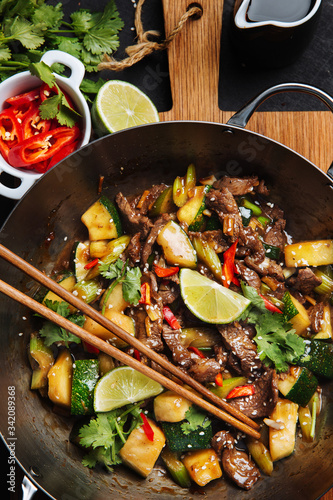 Top view of appetizing oriental spicy stir fry meat with zucchini and red pepper garnished with fresh lime and cilantro