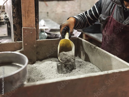 Crop male worker in apron and gloves scooping dry grey cement with plastic dustpan in workshop