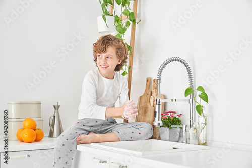 Blond child washing his hands in the kitchen sink to prevent any infection photo